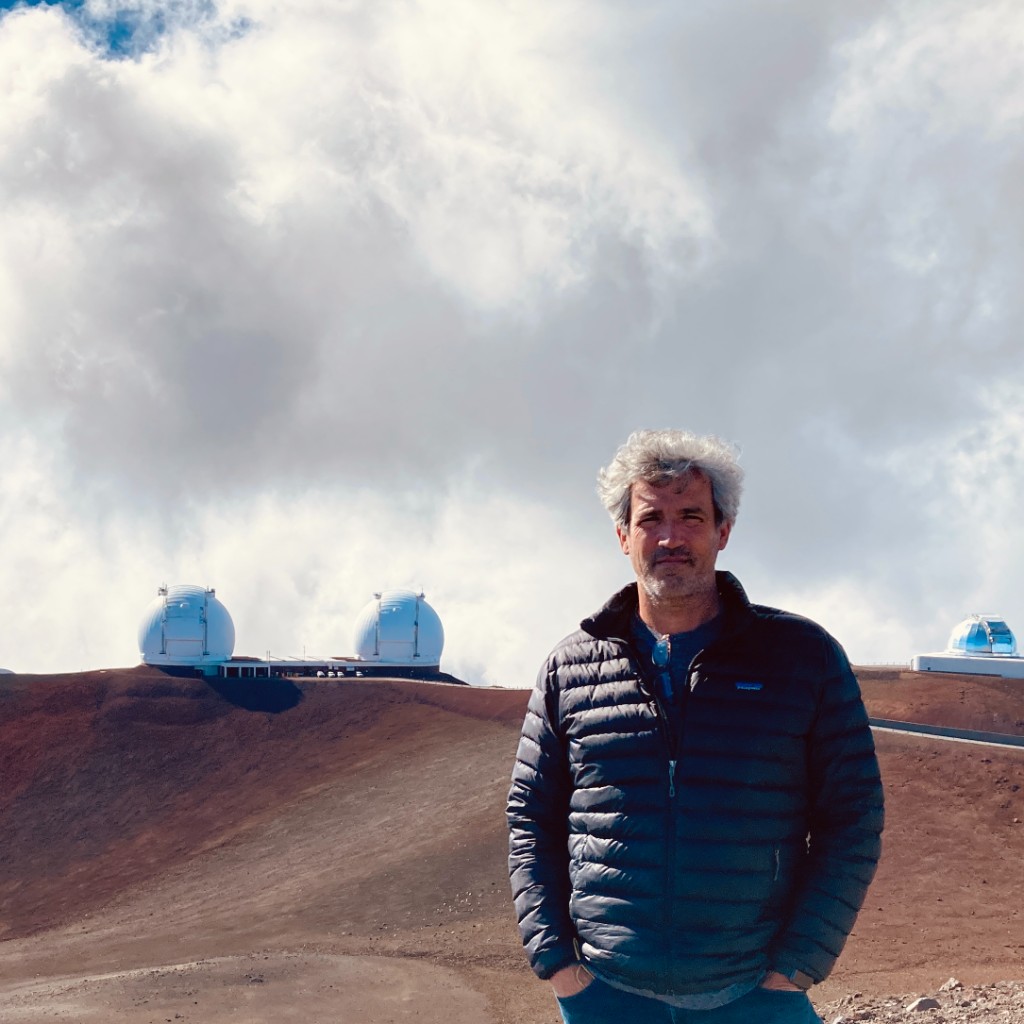 Jamie Roche in front of astronomical observatory domes on a volcanic mountain ridge