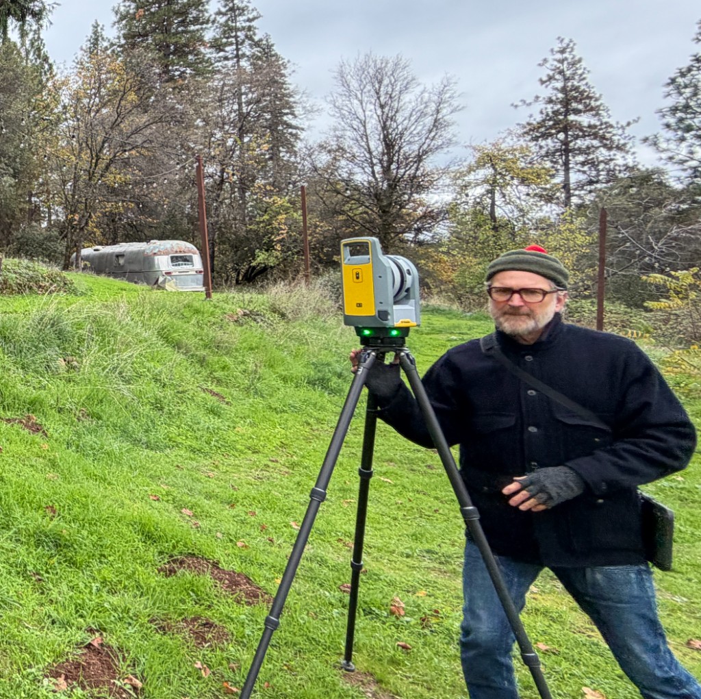 Kelly Green beside a tripod-mounted laser scanner on a grassy hillside