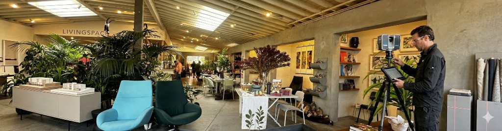 Wide interior of a furniture showroom with a technician operating a tripod-mounted 3D laser scanner and tablet
